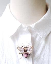 A Trovelore Bombus Bee Brooch Pin, detailed and hand embroidered, is pinned to the front of a crisp white collared shirt displayed on a mannequin.