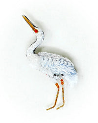 The Great Egret Brooch Pin by Trovelore is a hand embroidered accessory, handmade in India, featuring detailed white feathers, an orange beak, red eye, and slim orange legs—shown against a plain white background.
