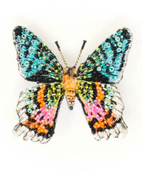 The Trovelore Madagascar Sunset Moth Brooch Pin is a hand-embroidered accessory adorned with blue, green, orange, pink, black, and white sequins and beads, beautifully showcased on a plain white background.