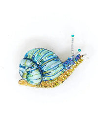 The Trovelore Roman Snail Brooch Pin is a handmade brooch with blue and green sequined shell, gold beaded body, and intricate embroidery, set against a plain white background.