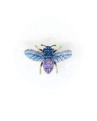 The Violet Carpenter Bee Brooch Pin by Trovelore features blue and purple sequins with detailed wings and antennae. Handmade in India, this beaded insect brooch adds a unique touch of artistry. Displayed on a plain white background.