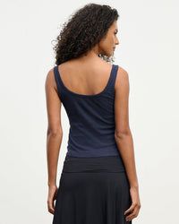 A woman with curly hair, seen from behind, wears the Velvet by Graham & Spencer Adelle Button Up Tank in Navy and a black skirt, standing against a plain light background.