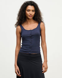 A woman with curly dark hair wears the Velvet by Graham & Spencer Adelle Button Up Tank in Navy and a black skirt, standing against a plain white background and looking at the camera with a slight smile.