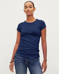 A person wears the Velvet by Graham & Spencer Jemma S/S Crew Neck Top in Midnight and blue jeans, standing against a plain light background, confidently looking at the camera with one hand relaxed by their side.