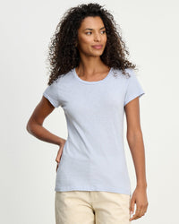 Woman with curly hair wears the Velvet by Graham & Spencer Odelia Scoop Neck Tee in Soho Sky and cream pants, posed against a white background.