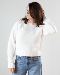 A person wears the White & Warren Cotton Blend Beachy Crew in White with blue jeans, standing against a plain background, touching their hair, which partially covers their face.