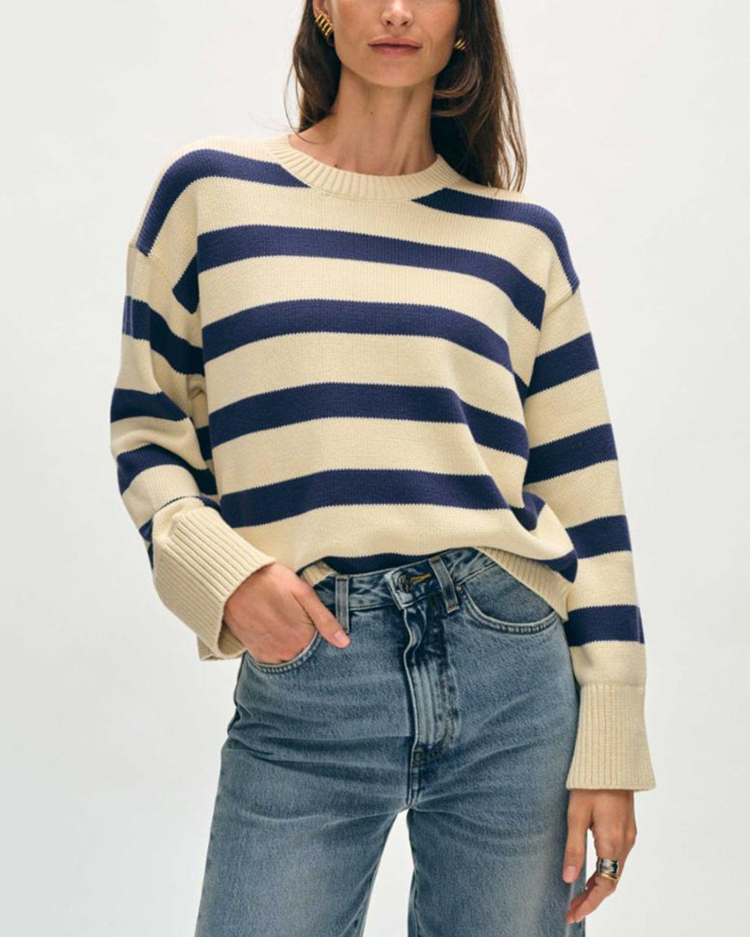 A woman wearing the White & Warren Organic Cotton Easy Crewneck in Ivory/Navy and high-waisted blue jeans stands with one hand in her pocket against a plain background.