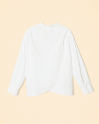 A white long-sleeve cotton poplin XiRENA Emile Top shown flat on a light beige background, featuring a curved overlapping back hem and buttoned cuffs—effortlessly stylish from behind.