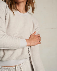 Wearing the perfectwhitetee Ziggy Inside Out Fleece L/S Shrunken Crew SS in Silver, a person stands with arms crossed against a plain background. The shrunken fit sweatshirt is made of inside out cotton fleece; face is partially out of frame.