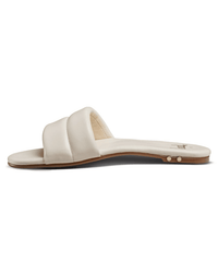 A side view of the beek.. Sugarbird in Eggshell: a minimalist leather slide sandal with a padded cream strap, thin sole, and subtle metallic accents—comfortable summer footwear with understated style.