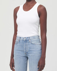 A person wearing the AGOLDE Poppy Tank in White with high-waisted light blue jeans stands against a plain light background. The image is cropped from shoulders to hips.