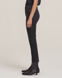 A person stands sideways against a light background wearing AGOLDE Riley Crop in Panoramic high-waisted skinny jeans, a dark top, and black ankle boots with a small heel.