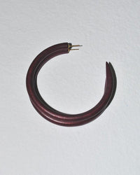 The B&L C Hoop in Large in Cocoa is a single, thick, dark maroon handmade mango wood earring with pointed ends and gold posts, shown on a textured white surface.