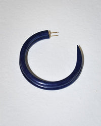 The B&L C Hoop in Large Reservoir, a dark blue, crescent-shaped earring hand carved from sustainably sourced mango wood with a gold post, is shown on a light textured surface.