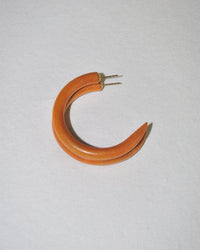 A single B&L C Hoop in Small in Leather Weekender, an orange crescent-shaped mango wood earring with a pointed end and two metal posts, is displayed on a plain white background.