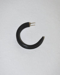 The B&L C Hoop in Small in Midnight Panther is a black, crescent-shaped earring with two metal prongs, elegantly displayed on a plain, light surface.