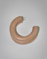 The B&L Large Chunk Hoop in Petal is a handmade, light brown mango wood earring with gold posts. It displays natural charm and timeless style while resting on a light gray surface, softly casting a shadow. Sustainably sourced.