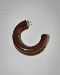 A single Large Chunk Hoop in Raisin by B&L, a brown crescent-shaped mango wood earring with a broken post, rests on a plain white surface and casts a soft shadow to the right.