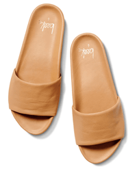 The Gallito in Honey slides by beek. feature tan leather with wide, smooth straps, flat soles, and a memory foam footbed for comfort. "beek." is printed in white on the insole. They're shown against a white background.