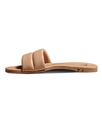 The beek.. Sugarbird in Beach is a tan flat slide sandal with a cushioned wide strap, memory foam sole, and slight heel, shown from the side on a white background.