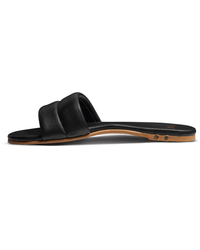 The beek.. Sugarbird in Black is a flat slide sandal with a padded single strap, thin brown sole, and molded footbed for comfort, shown from the side on a white background.