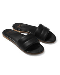 The beek.. Sugarbird in Black is a pair of comfortable leather slide sandals featuring wide padded straps, flat soles, a slightly arched memory foam insole, and gold rivet accents on the light brown outsole.