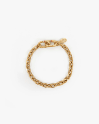 The Clare V. Charm Chain Bracelet in Vintage Gold features oval links, a large clasp, and a small engraved tag, beautifully shown on a white background.
