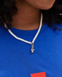 A person wears a blue shirt and Clare V.’s Mini Checker Whistle Charm in Black/Cream/Vintage Gold as a necklace. Only the lower face and neck are visible.