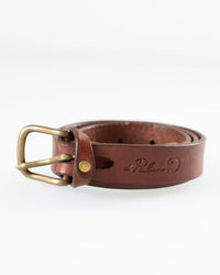 The Depalma Handsewn 1 inch Mon Senor Belt in Bark features genuine brown leather, a solid brass buckle, and an engraved logo, shown coiled against a plain white background.
