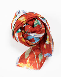 The Épice Meadow Orchids Scarf in Copper, featuring a vibrant floral pattern on a copper background, is rolled neatly with one end extended outward and displayed on a white surface.