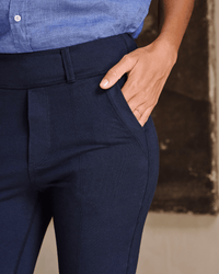 A person in a blue button-up shirt and Frank & Eileen Murphy Pant in British Royal Navy stands with one hand in their pocket, displaying neatly manicured fingers and a slim ring.