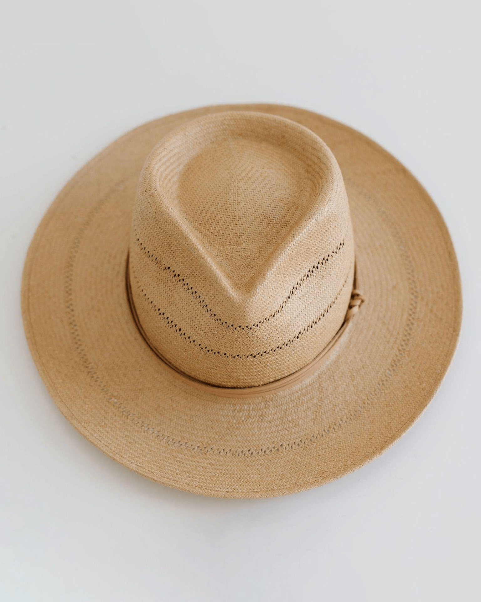 The Arlo Honey Straw Teardrop Fedora by Gigi Pip features a tan, wide brim, creased crown, handwoven venting, nude band, and adjustable strap. Displayed on a plain white background.