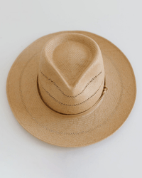 The Arlo Honey Straw Teardrop Fedora by Gigi Pip features a tan, wide brim, creased crown, handwoven venting, nude band, and adjustable strap. Displayed on a plain white background.