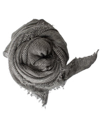 The Grisal Love Cashmere Scarf in Charcoal X Milk, made from luxury yarn with frayed edges and gray-white stripes, is rolled into a spiral and shown against a white background.