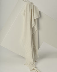 The Love Cashmere Scarf in Milk by Grisal—a light beige, fringed accessory—is draped over a white geometric structure against a neutral background.