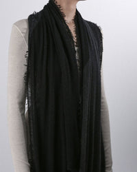 A person wears a light-colored long-sleeve shirt and a Grisal Love Duo Cashmere Scarf in Charcoal & Black draped around their neck. The photo is cropped from the shoulders down, so their head is not visible.