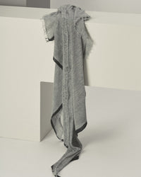 The Grisal Rosa Cascade Cashmere Scarf in Heather Grey X Charcoal drapes over a large white geometric structure in a minimalist setting.