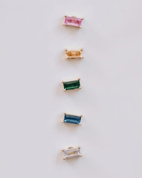 The JaxKelly Rainbow Baguette Earring Set features five rectangular cubic zirconia studs in gold, with pink, light brown, green, blue, and clear stones arranged vertically on a light background.