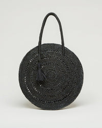 The Cercle Medium in Noir by Maison N.H Paris is a round, black woven straw handbag with two handles and a black tassel, shown upright against a plain light background.