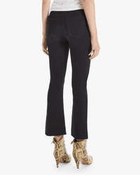 A person wearing Mother’s The Hustler Ankle Fray in Not Guilty jeans with a raw hem and beige snakeskin high-heeled boots, shown from the back and styled with a white top against a light background.