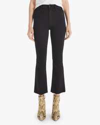 A person wears Mother’s The Hustler Ankle Fray in Not Guilty—black high rise flare jeans with a raw hem—paired with a white top and yellow snakeskin ankle boots, standing against a white background.