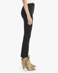 A person stands in profile wearing Mother’s The Hustler Ankle Fray in Not Guilty—high-rise flare jeans with a black denim wash—paired with a white shirt and yellow snakeskin high-heeled ankle boots, against a plain white background.