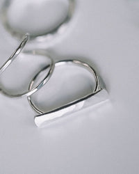 Close-up of two minimalist Nashelle sterling silver rings on a light surface; one is plain and circular, and the other is the Nashelle Faceted Bar Ring in Silver, featuring a handmade horizontal rectangular bar design.