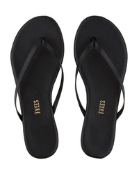 A pair of Tkees Liners Flip Flops in Sable, crafted from quality cowhide leather with thin straps and the Tkees brand name printed in gold on the insole, shown from above.