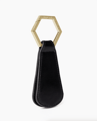 The Drop in Black/Gold by TopTote is a sleek leather key holder with a gold hexagonal ring, shown upright on a white background—a stylish accessory to keep your essentials organized.