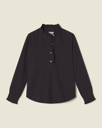 The Breezy Blouse in Black by Trovata Birds of Paradis is a 100% cotton long-sleeve top with a ruffled back, high ruffled collar, partial button-down front, and ruffled cuffs, shown on a plain light background.