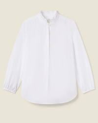 The Sara B Henley Shirt in White by Trovata Birds of Paradis is a 100% cotton long-sleeve blouse with a ruffle collar, button placket, and gathered cuffs, shown on a light beige background.