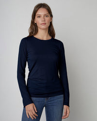 A woman with long brown hair wears the Velvet by Graham & Spencer Zofina in Midnight pullover and blue jeans, standing against a light gray background and looking at the camera with a neutral expression.