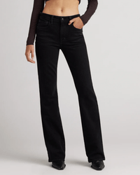 Person wearing Edwin Lark in Ramble mid-rise boot jeans, a cropped long-sleeve top, and black pointed-toe shoes stands against a plain light background with one hand in their pocket.