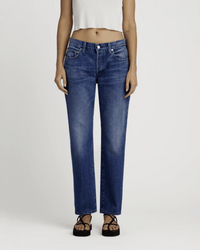 A person wears the Edwin Simone in Idle indigo wash straight leg jeans, a white cropped sleeveless top, and black sandals, standing against a plain light background.